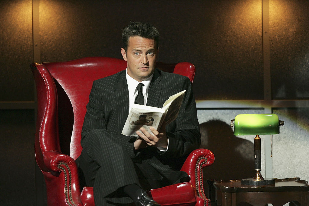 Matthew Perry, pe un fotoliu, în timp ce citește o carte