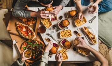 Mai multe persoane care stau la o masă și consumă alimente și băuturi procesate care pot fi periculoase pentru sănătate