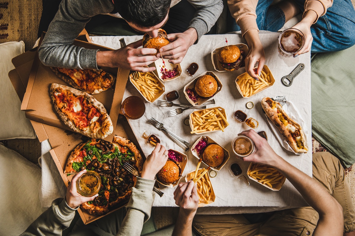 Mai multe persoane care stau la o masă și consumă alimente și băuturi procesate care pot fi periculoase pentru sănătate
