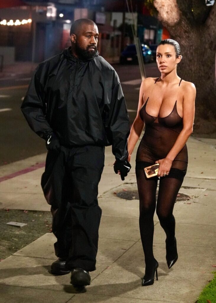 Bianca Censori și Kanye West în timp ce se plimbă de mână pe stradă, iar Bianca poartă i ținută complet transparentă