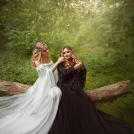 Două femei îmbrăcate în rochii lungi, albă și neagră