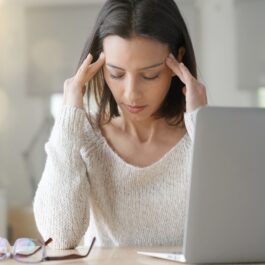 O femeie care își ține mâinile pe cap și privește la laptop