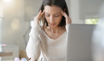 O femeie care își ține mâinile pe cap și privește la laptop