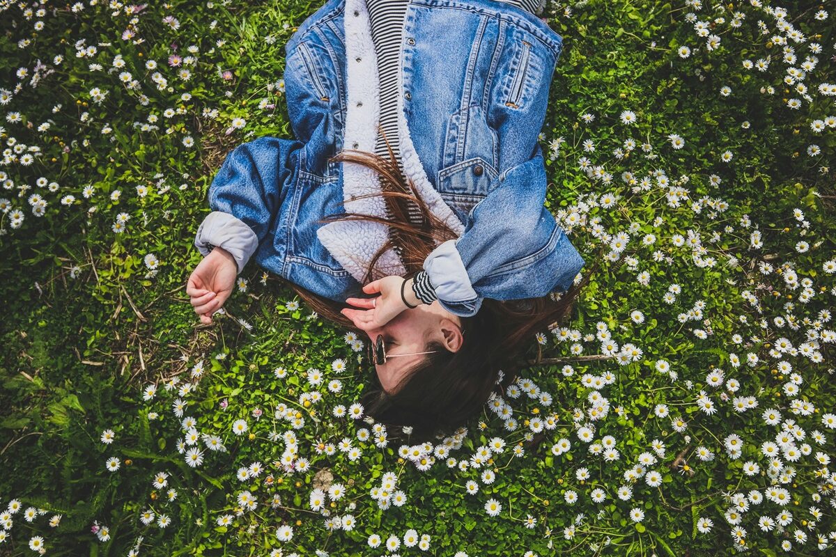 O tânără care poartă o jachetă de blugi și stă pe iarba înflorită