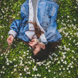O tânără care poartă o jachetă de blugi și stă pe iarba înflorită