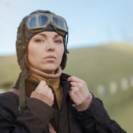 Femeie pilot cu cască pe cap și cu un avion în spate