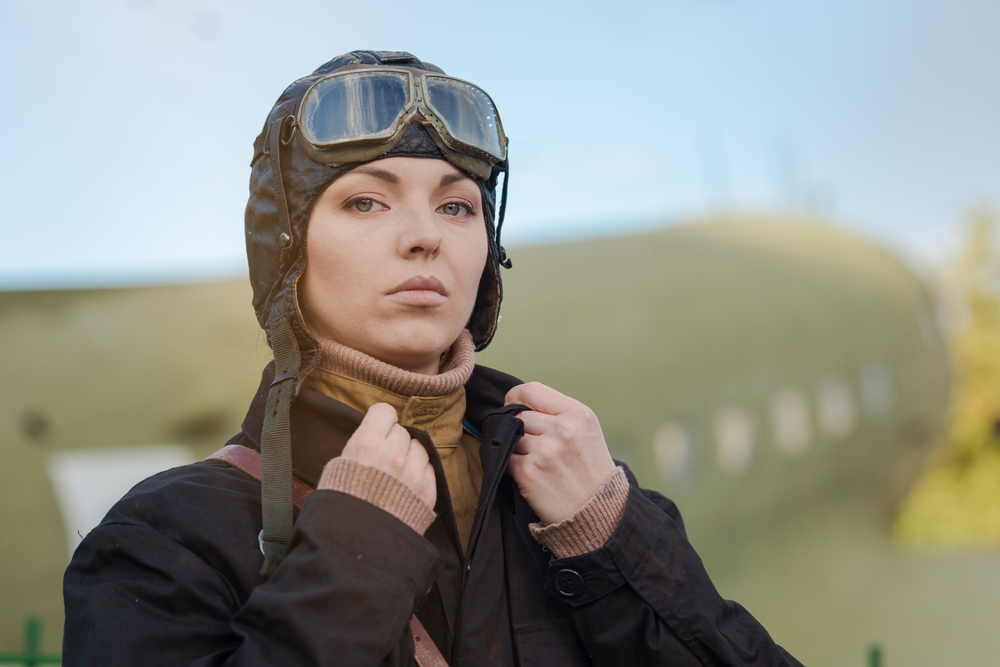 Femeie pilot cu cască pe cap și cu un avion în spate