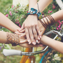 mâini unite ale unor prietene deasupra unei biciclete pe un câmp