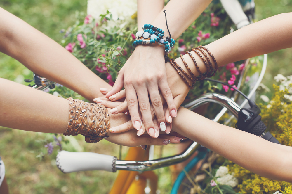 mâini unite ale unor prietene deasupra unei biciclete pe un câmp