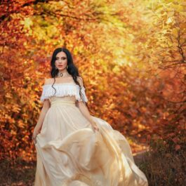 O femeie frumoasă care poartă o rochie aurie și pășește cu încredere într-o pădure în peisaj de toamnă pentru a ilustra una dintre acele zodii care nu suportă nedreptatea
