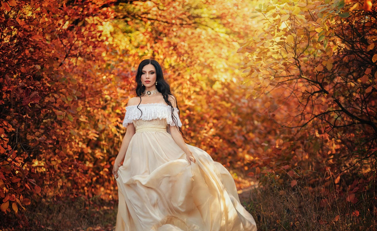 O femeie frumoasă care poartă o rochie aurie și pășește cu încredere într-o pădure în peisaj de toamnă pentru a ilustra una dintre acele zodii care nu suportă nedreptatea