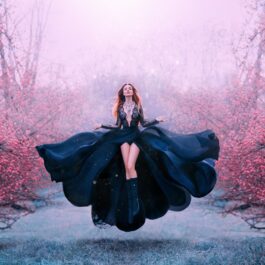 O femeie frumoasă care poartă o rochie neagră și levitează într-o pădure cu copaci cu flori roz