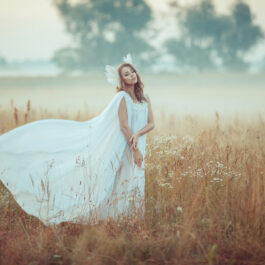 O femeie îmbrăcată în rochie albă, într-un câmp