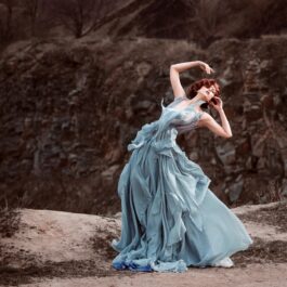 O femeie frumoasă care poartă o rochie gri și dansează într-o zonă pustie pentru a ilustra una dintre acele zodii care trec printr-o schimbare majoră în martie 2024