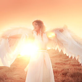 O femeie cu aripi de înger care stă în lumina apusului de soare