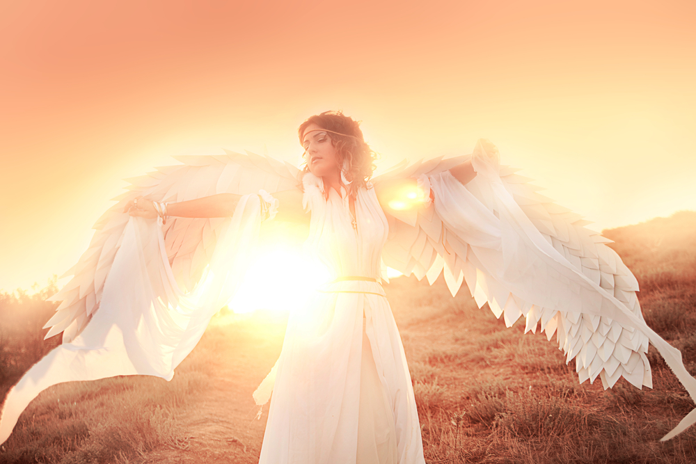 O femeie cu aripi de înger care stă în lumina apusului de soare