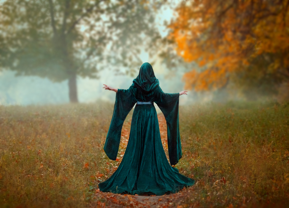 femeie îmbrăcată într-o pelerină stă într-o pădure
