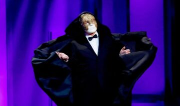 Mike Mayers în timp ce poartă o mască și se află pe senă la gala Premiilor Academiei