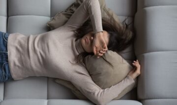 O femeie care stă obosită, cu mâna la ochi, pe o canapea