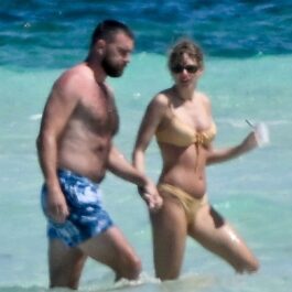 Taylor Swift și Travis Kelce în timp ce se țin de mână și se plimbă pe plajă