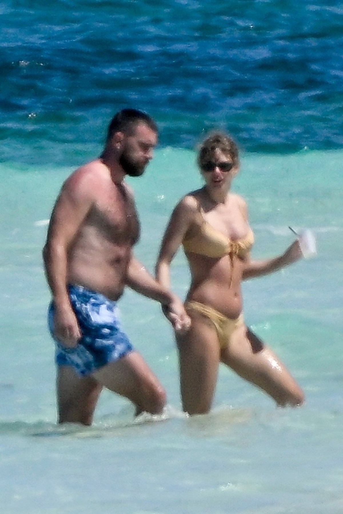 Taylor Swift și Travis Kelce în timp ce se țin de mână și se plimbă pe plajă