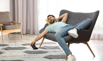 Un bărbat care stă pe o canapea, cu telecomanda în mână, care cască