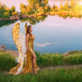 O femeie într-o rochie elegantă, cu aripi de înger, pe marginea unui lac