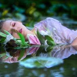 O femeie într-o rochie albă, care plutește cu o floare pe luciul apei