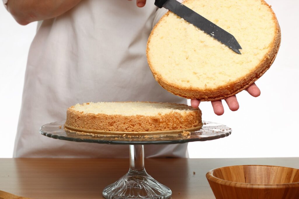 Persoană secționând blatul de tort în două cu un cuțit zimțat
