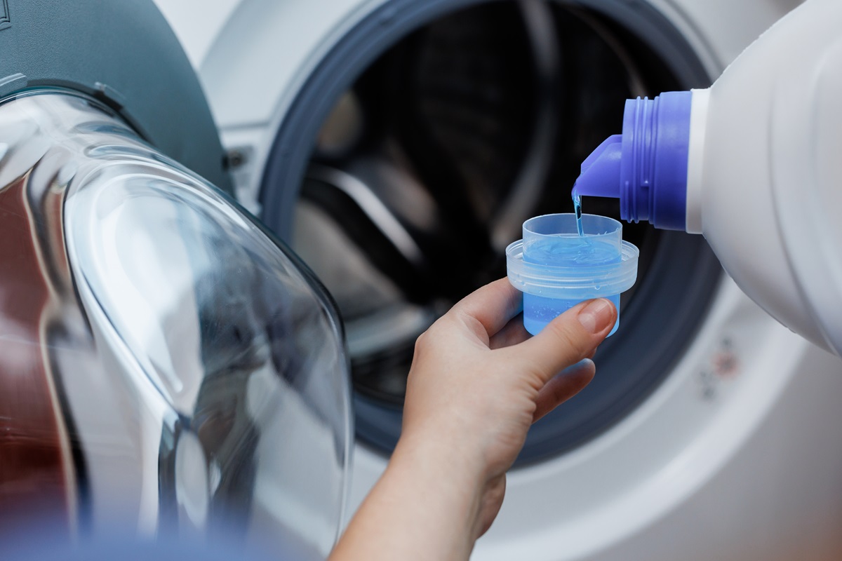 O femeie care pune detergent lichid într-un căpăcel pentru a-l adăuga în mașina de spălat