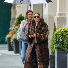 Jennifer Lopez în timp ce se plimbă pe stradă într-o haină de blană, iar asistenta ei ține o umbrelă