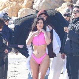 Kim Kardashian într-un costum de baie roz în timp ce este urmată de o întreagă echipă de fotografi pe plajă