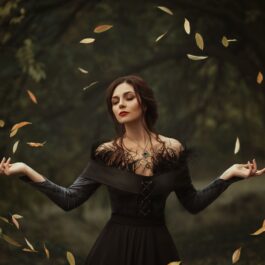 O femeie frumoasă care poartă o rochie neagră și ține într-un cerc armonios mai multe frunze aurii