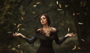 O femeie frumoasă care poartă o rochie neagră și ține într-un cerc armonios mai multe frunze aurii