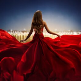 O femeie frumoasă care poartă o rochie roșie și privește către orizont pentru a ilustra una dintre zodiile ambițioase în carieră