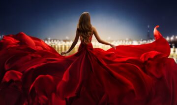 O femeie frumoasă care poartă o rochie roșie și privește către orizont pentru a ilustra una dintre zodiile ambițioase în carieră